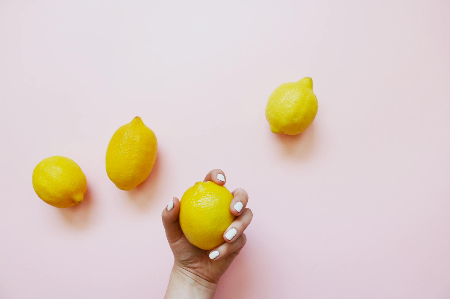 A hand holding a lemon on a soft pink background, representing the fresh approach to rediscovering pleasure with a partner