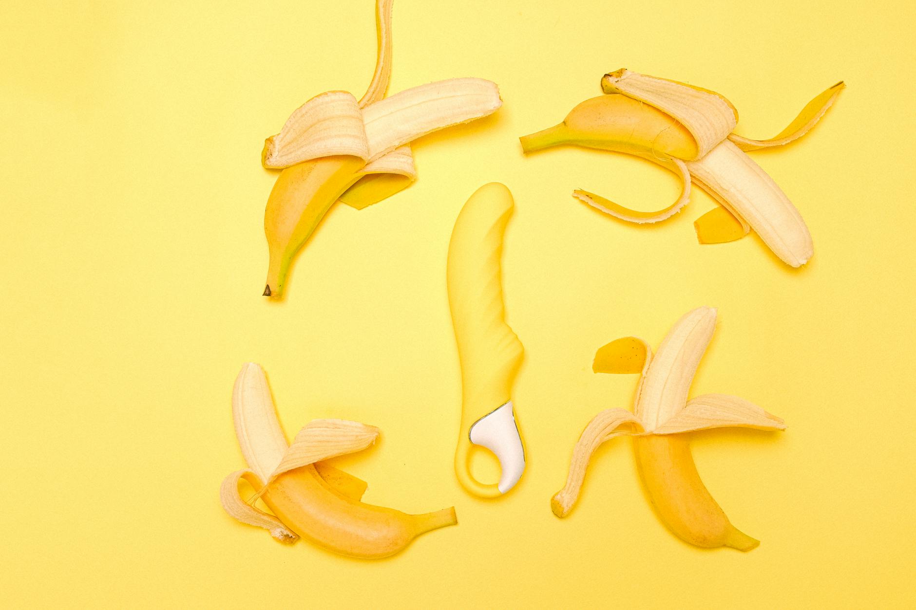 Creative flat lay of a yellow silicone vibrator surrounded by fresh lemons on a bright yellow background