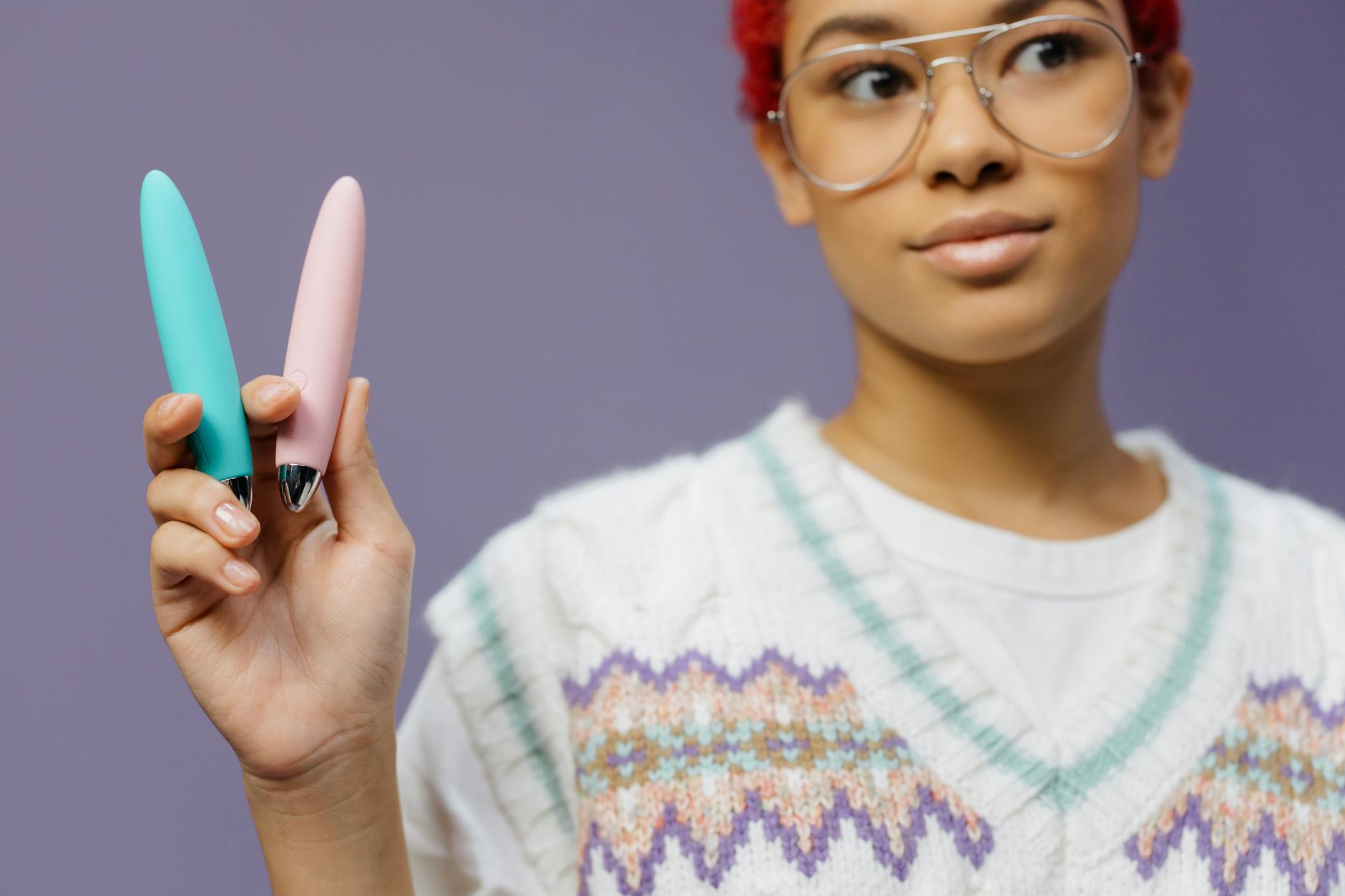 Woman holding colorful vibrators against a purple background, demonstrating pleasure tools