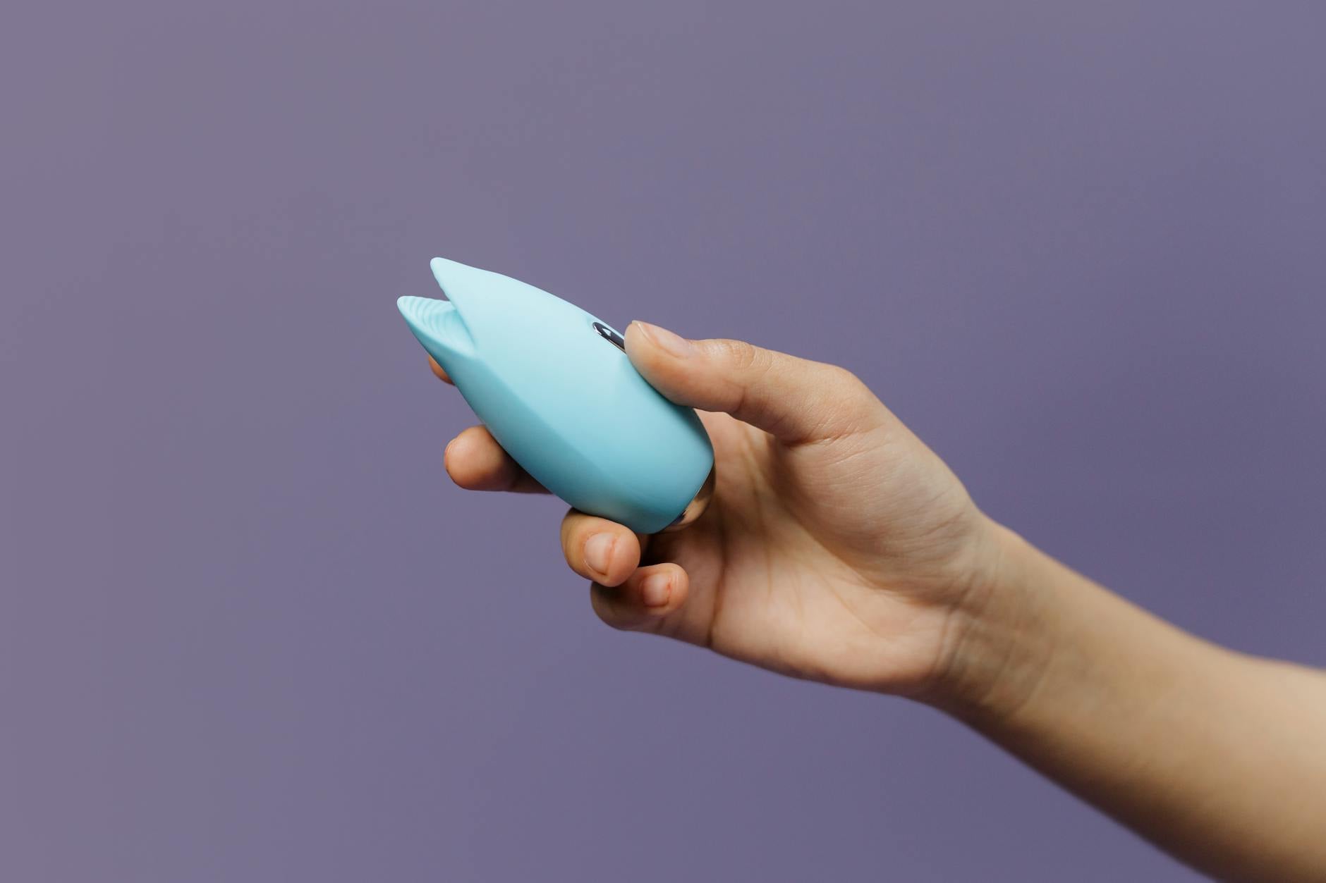 Woman holding a pink clitoral vibrator with books nearby, intimate personal setting