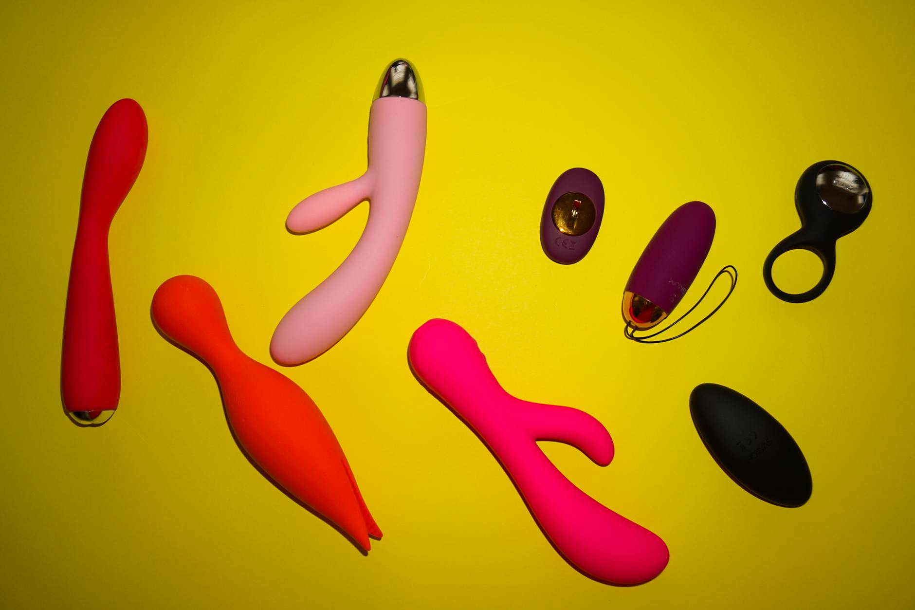 Colorful sex toys arranged on a bright yellow surface, showcasing diverse shapes and designs